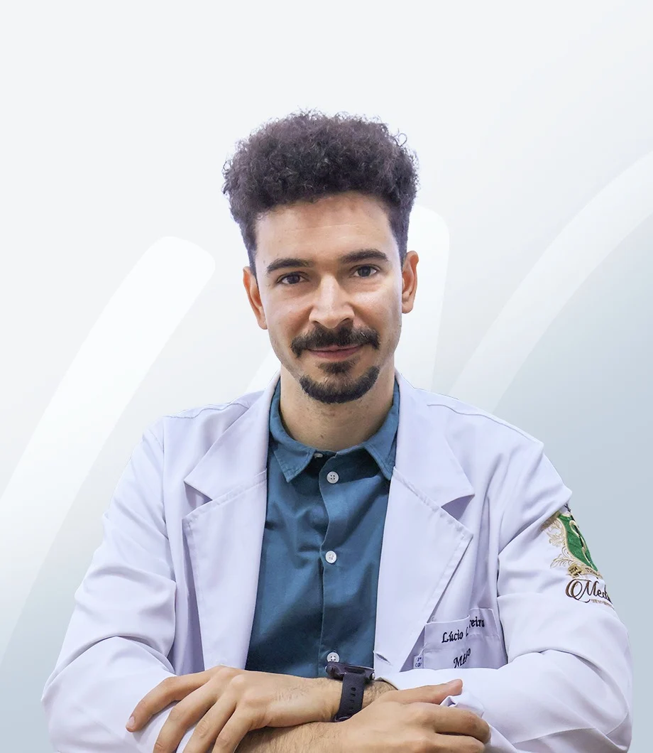 Dr. Lúcio Moreira, de jaleco branco e camisa azul, com os braços cruzados sobre a mesa.
